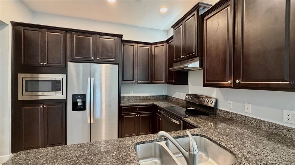 A kitchen featuring dark wood cabinets, granite countertops, and stainless steel appliances — 8348 TAVISTOCK LAKES BOULEVARD, ORLANDO, FL