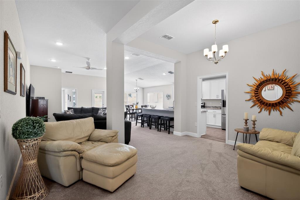A living room with beige leather furniture, carpeted floors, and a view into the kitchen — 17941 SW 66TH PLACE, DUNNELLON, FL
