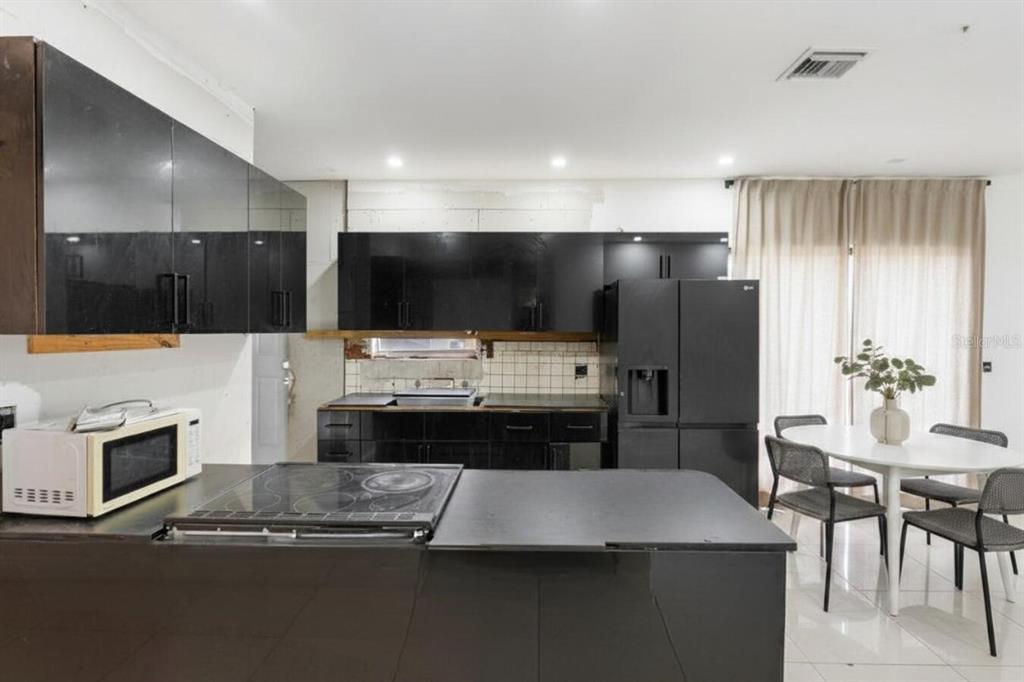 A modern kitchen features black cabinetry, a black island cooktop, and an adjacent dining area — 1829 5TH, MIAMI, FL