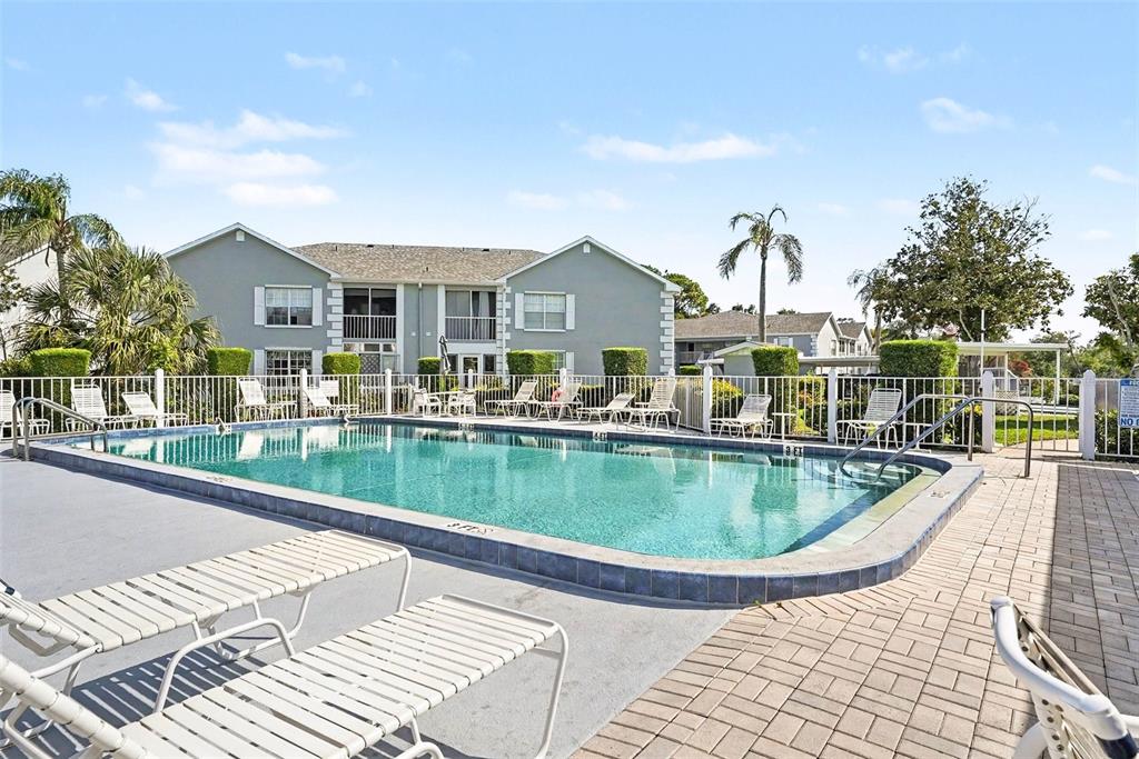 A swimming pool sits in front of a multi-story apartment building with lounge chairs nearby — 12049 HOOSIER COURT UNIT 203, HUDSON, FL