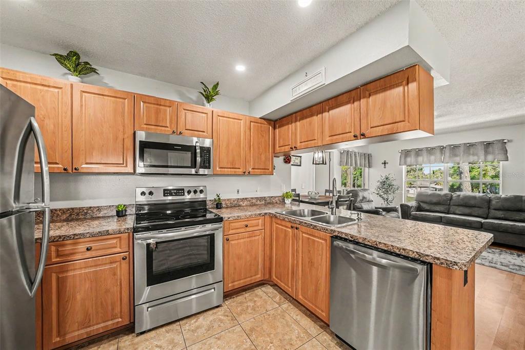 A kitchen with wood cabinets, granite countertops, and stainless steel appliances overlooks a living area — 12049 HOOSIER COURT UNIT 203, HUDSON, FL