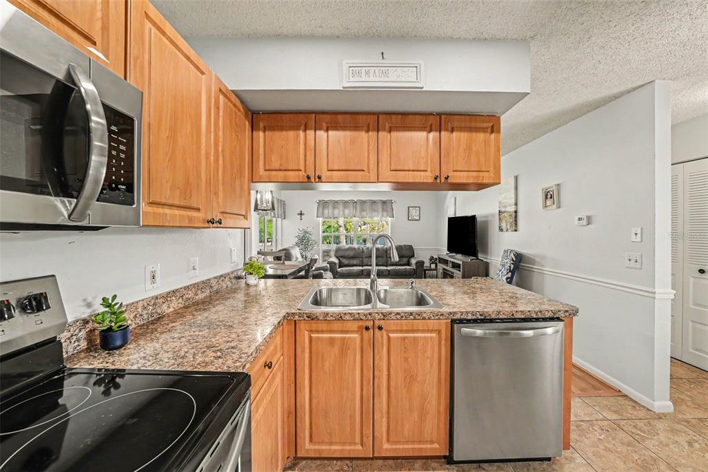 A kitchen with wood cabinets, granite countertops, and stainless steel appliances overlooks a living area — 12049 HOOSIER COURT UNIT 203, HUDSON, FL