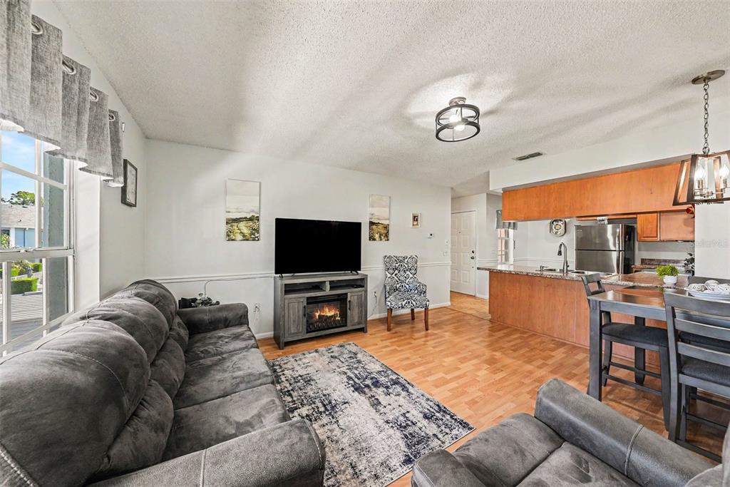 A living room with a grey sofa, fireplace TV stand, and an adjacent kitchen area — 12049 HOOSIER COURT UNIT 203, HUDSON, FL