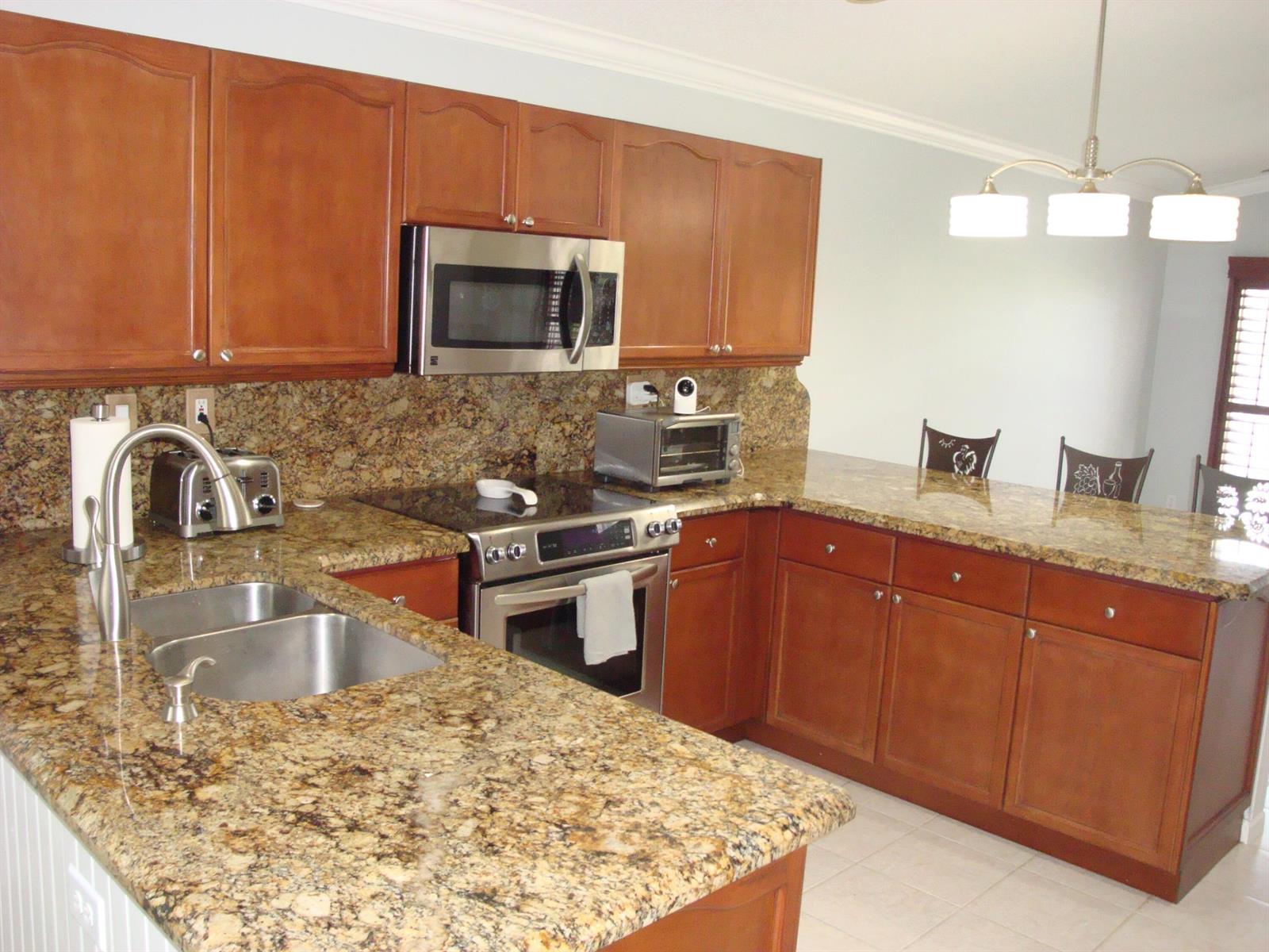 A kitchen with wood cabinets, granite countertops, stainless steel appliances, and a breakfast bar — 6304 Barton Creek Circle, Lake Worth FL 33463, LAKE WORTH, FL