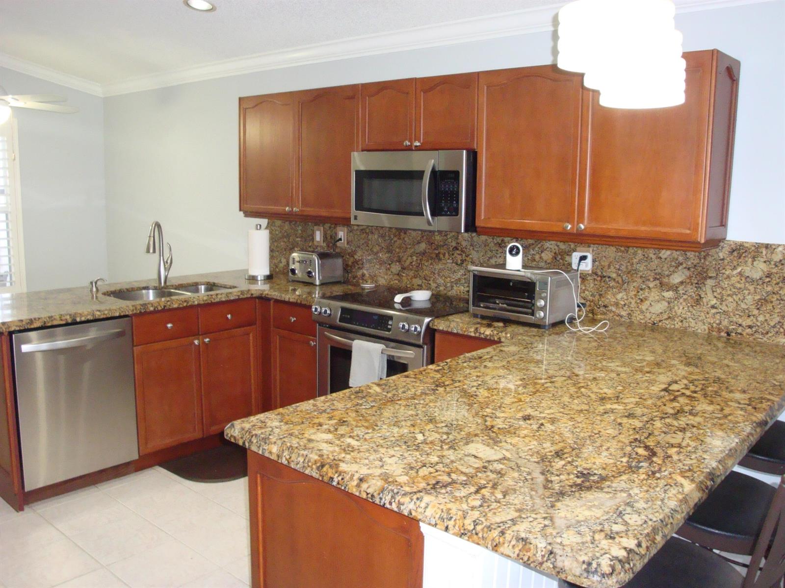A kitchen with wood cabinets, granite countertops, stainless steel appliances, and a breakfast bar — 6304 Barton Creek Circle, Lake Worth FL 33463, LAKE WORTH, FL