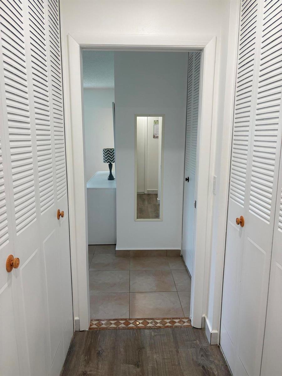 A hallway with louvered closet doors leads to a tiled room containing a wall mirror — 2522 Emory Drive E # A, West Palm Beach FL 33415, WEST PALM BEACH, FL