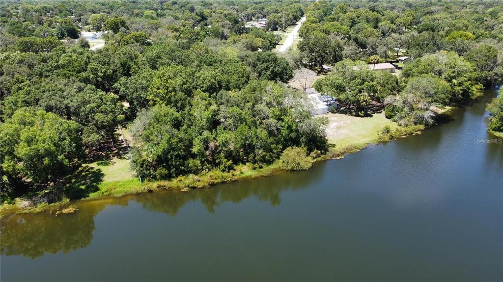 An aerial view shows a house nestled among dense trees beside a large lake — 12102 PARKWOOD ST, HUDSON, FL