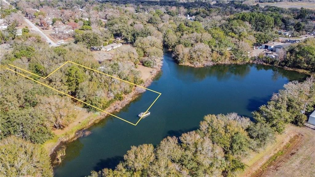 An aerial view shows a wooded waterfront lot outlined in yellow next to a lake — 12102 PARKWOOD ST, HUDSON, FL