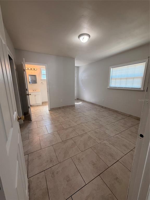 A bedroom with light-colored tile flooring and an attached bathroom visible through an open door — 110 FOREST AVENUE UNIT 8, DAVENPORT, FL
