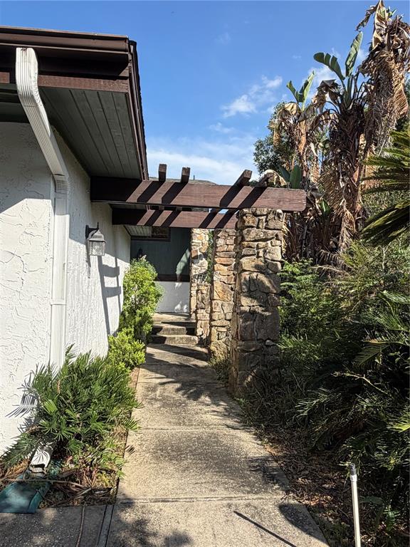 A concrete walkway leads toward a stone pillar and a wooden pergola beside a house — 8 CANTERBURY DRIVE, HAINES CITY, FL