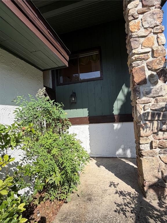 A stone pillar stands beside a concrete walkway leading to a green-sided house exterior — 8 CANTERBURY DRIVE, HAINES CITY, FL