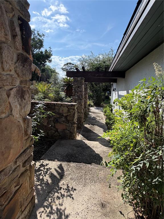 A stone wall and a wooden pergola frame a concrete walkway leading toward a house — 8 CANTERBURY DRIVE, HAINES CITY, FL