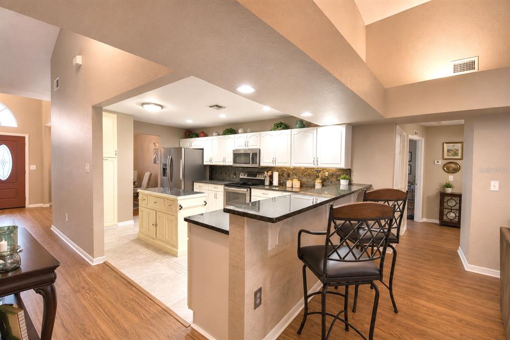 A kitchen with white cabinets, a granite-topped island, and a breakfast bar with two chairs — 659 SIERRA CIRCLE, DAVENPORT, FL