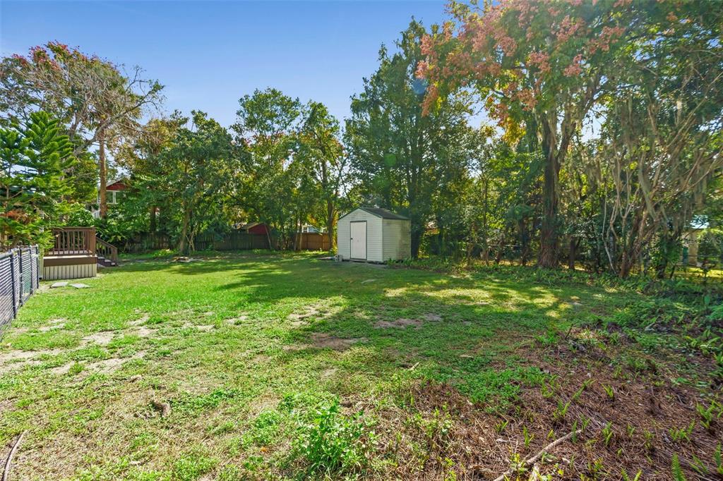 A grassy backyard features a small storage shed, mature trees, and a wooden deck — 210 W UNIVERSITY AVENUE, DELAND, FL