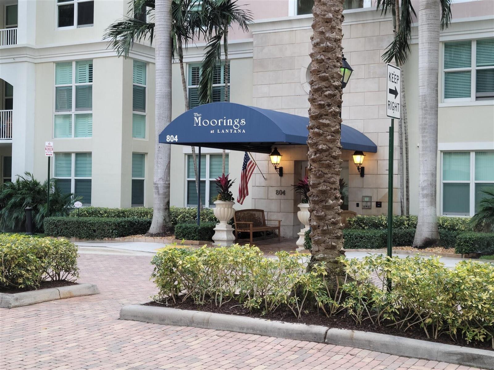 The exterior entrance of a multi-story building features a blue awning and palm trees — 804 E Windward Way # 508, Lantana FL 33462, LANTANA, FL