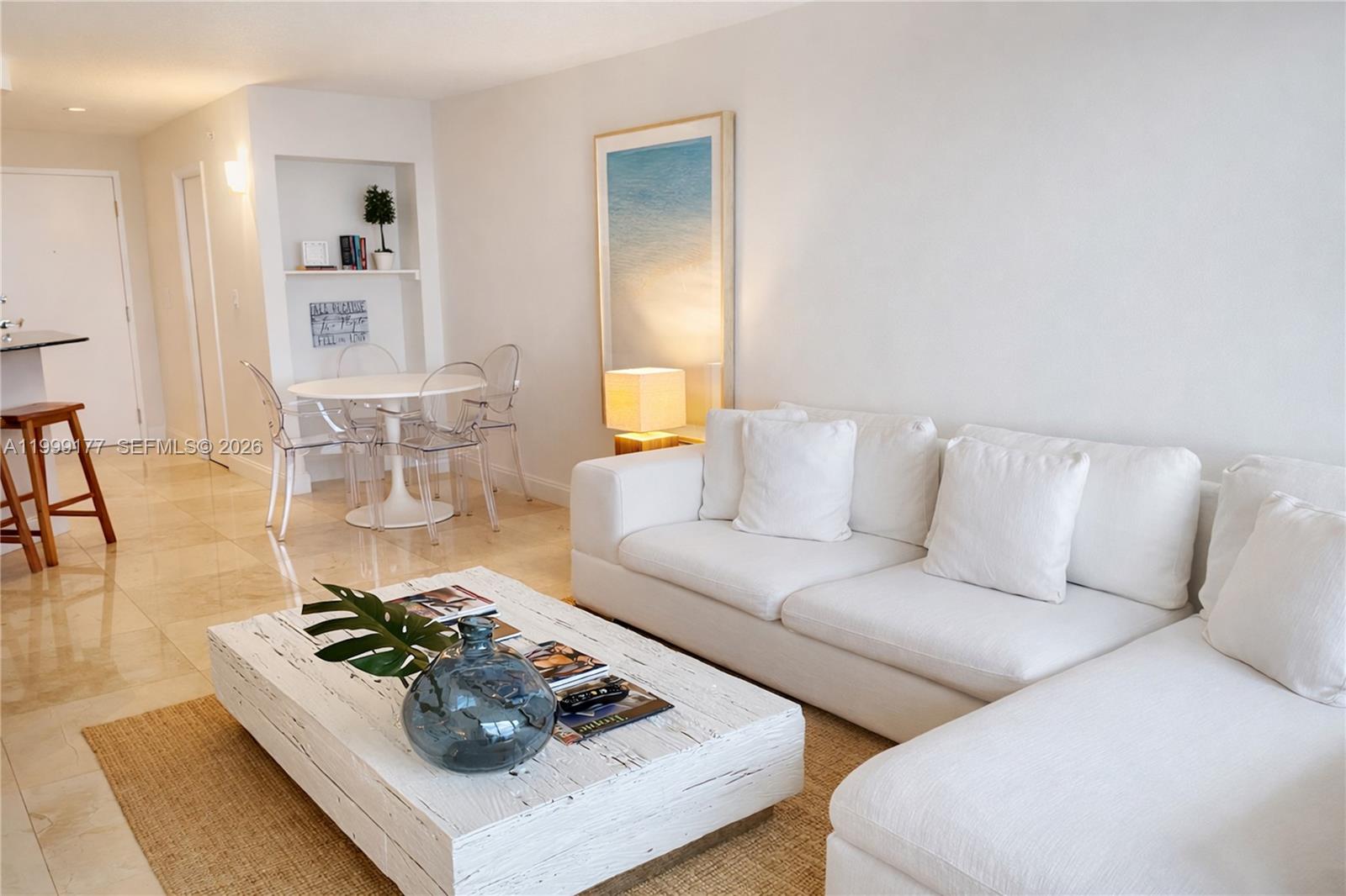 A living room features a white sectional sofa, a rustic coffee table, and a dining area — 6917 Collins Ave # 1611, Miami Beach FL 33141, MIAMI BEACH, FL