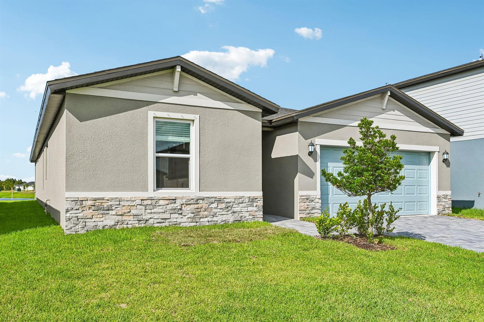 A single-story house with a gray stucco exterior, stone veneer base, and a blue garage — 14503 SW New Dawn Road, FL 34956, FL