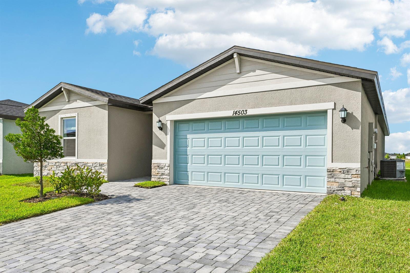 A single-story house with a light blue garage door, stone accents, and a paver driveway — 14503 SW New Dawn Road, FL 34956, FL