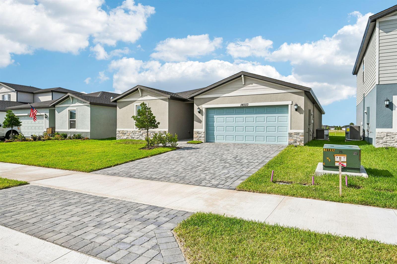 A single-story suburban house with a paved driveway, light blue garage door, and stone accents — 14503 SW New Dawn Road, FL 34956, FL