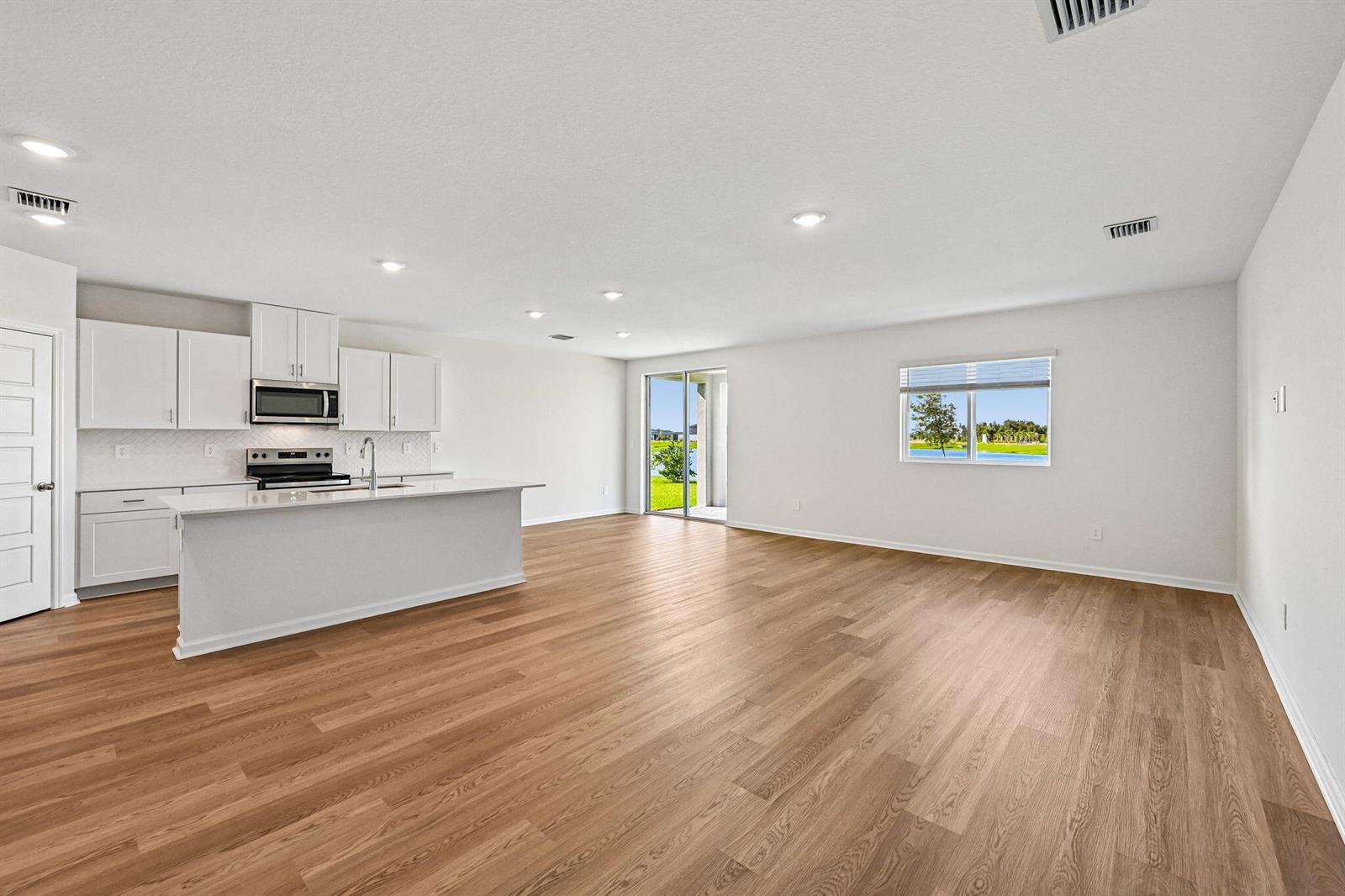 An open-concept kitchen and living area features white cabinets, a center island, and wood flooring — 14503 SW New Dawn Road, FL 34956, FL