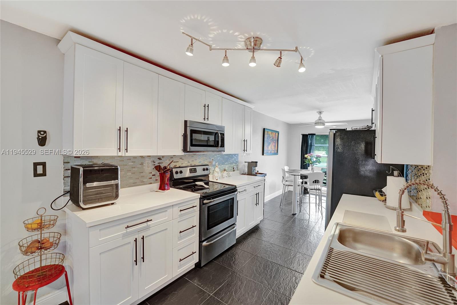 A kitchen features white cabinets, stainless steel appliances, a mosaic backsplash, and dark tile flooring — 3301 Raleigh St # 4E, Hollywood FL 33021, HOLLYWOOD, FL