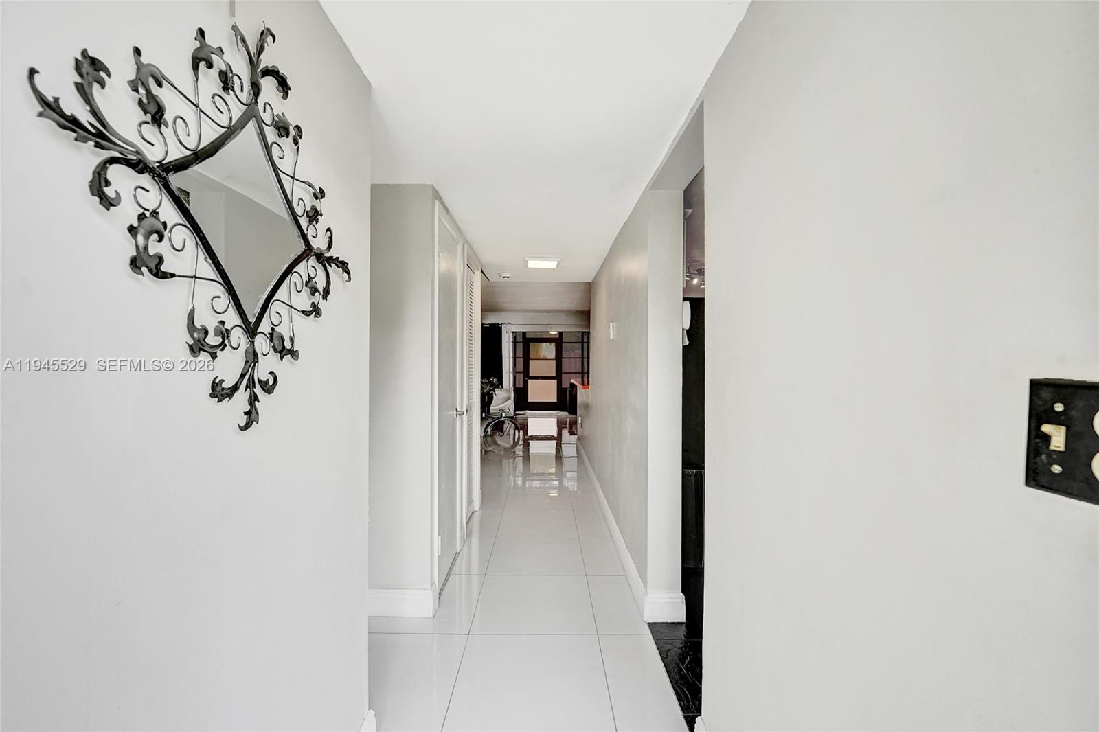A hallway with white tiled floors, light gray walls, and a decorative wall mirror — 3301 Raleigh St # 4E, Hollywood FL 33021, HOLLYWOOD, FL