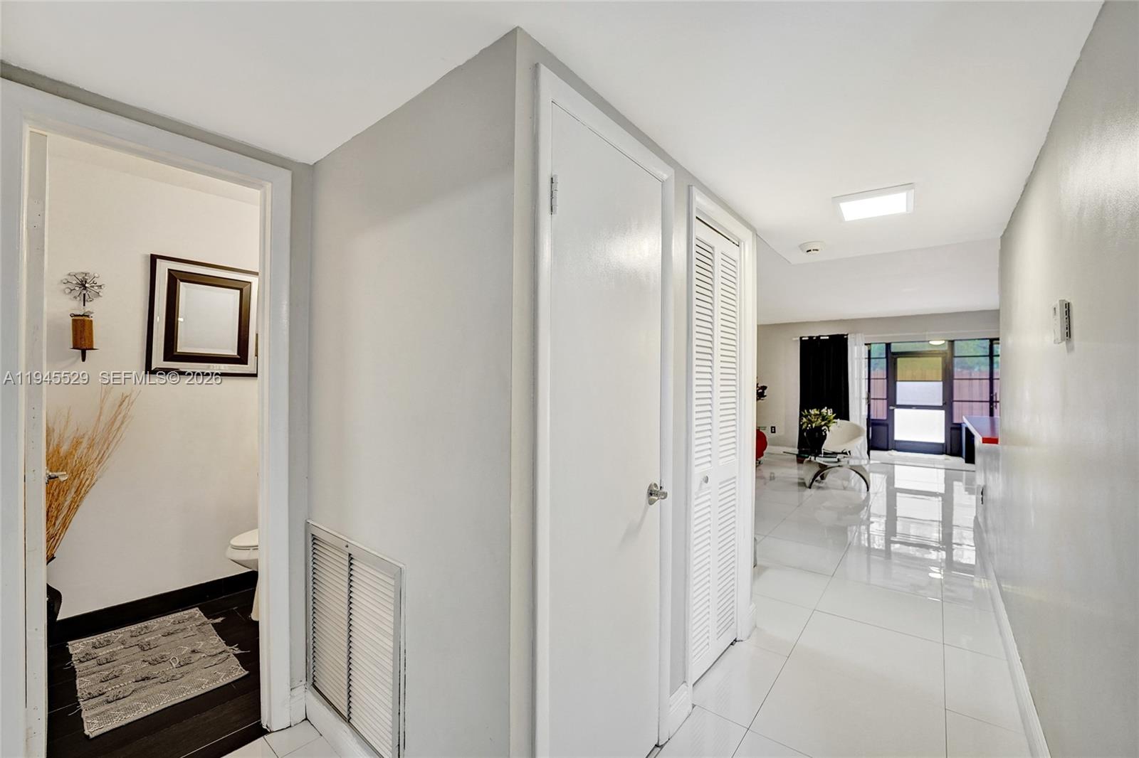 A hallway with white tile floors leads to a living area and a small bathroom — 3301 Raleigh St # 4E, Hollywood FL 33021, HOLLYWOOD, FL