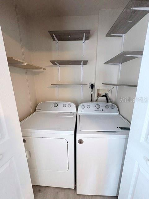 A laundry closet contains a white washer and dryer with open shelving mounted on the walls — 13756 ORANGE SUNSET DRIVE UNIT 101, TAMPA, FL