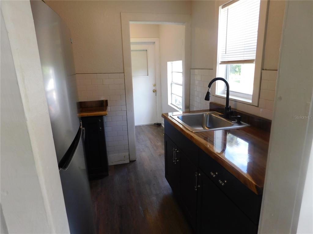A kitchen features a stainless steel refrigerator, dark cabinets, wood countertops, and white subway tile — 1009 17TH STREET S, ST PETERSBURG, FL