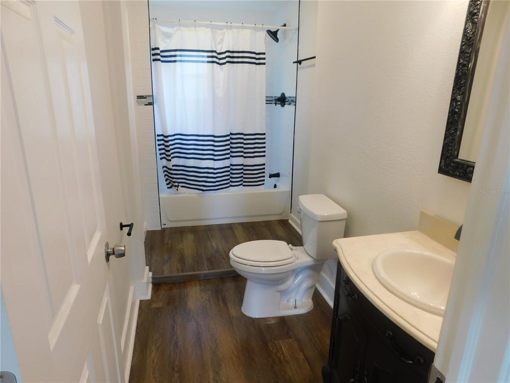 A bathroom features wood-look flooring, a white toilet, a vanity, and a shower-tub combination — 1009 17TH STREET S, ST PETERSBURG, FL