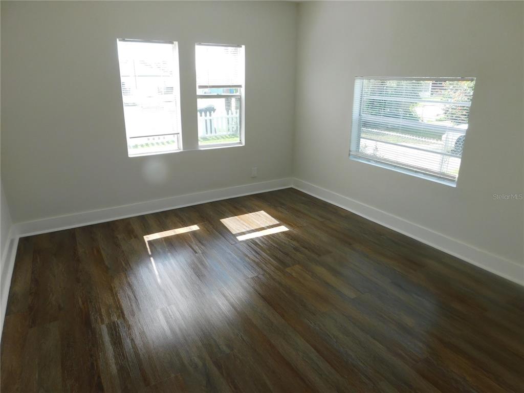 An empty room features wood-look flooring, white walls, and three windows with blinds — 1009 17TH STREET S, ST PETERSBURG, FL