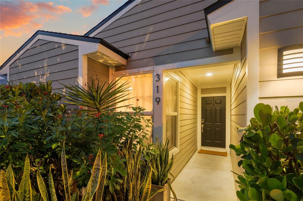 The exterior of a house features gray siding, a dark front door, and lush landscaping — 319 BEARDED OAKS CIRCLE, SARASOTA, FL