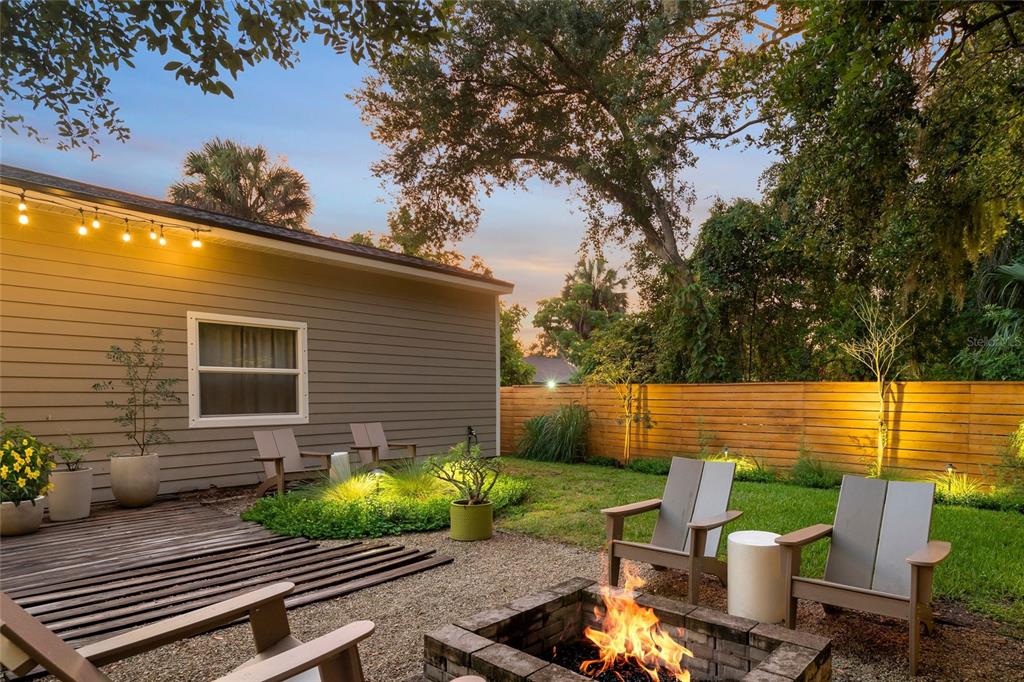 A backyard patio features a stone fire pit, gravel ground, and wooden chairs at dusk — 319 BEARDED OAKS CIRCLE, SARASOTA, FL