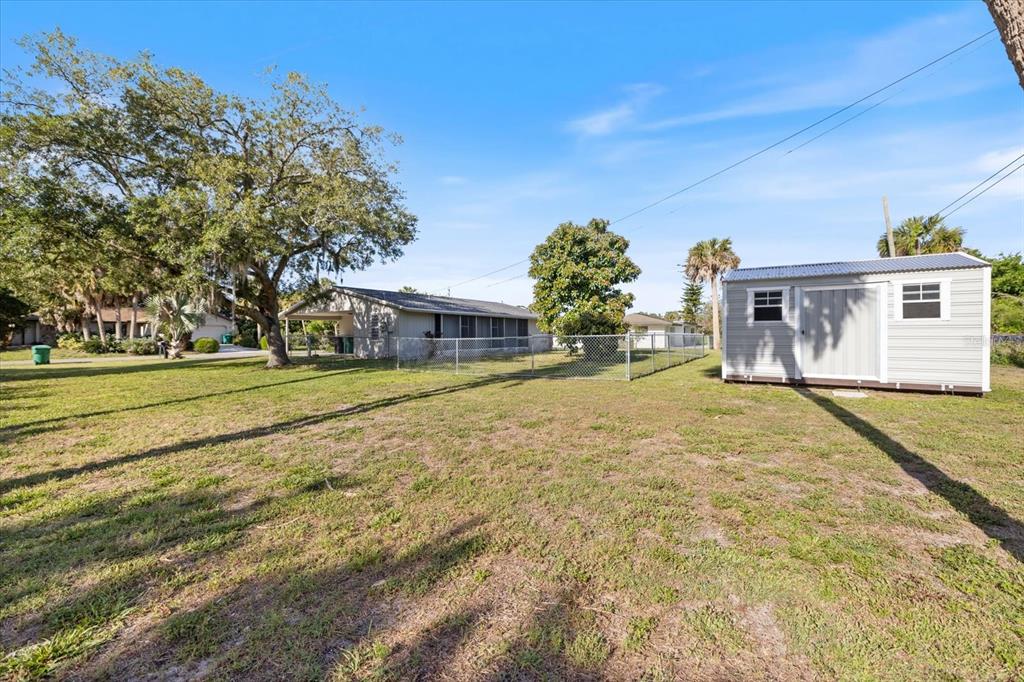 A grassy backyard features a chain-link fence, a storage shed, and a house with a carport — 1184 BARBOUR AVENUE, PORT CHARLOTTE, FL