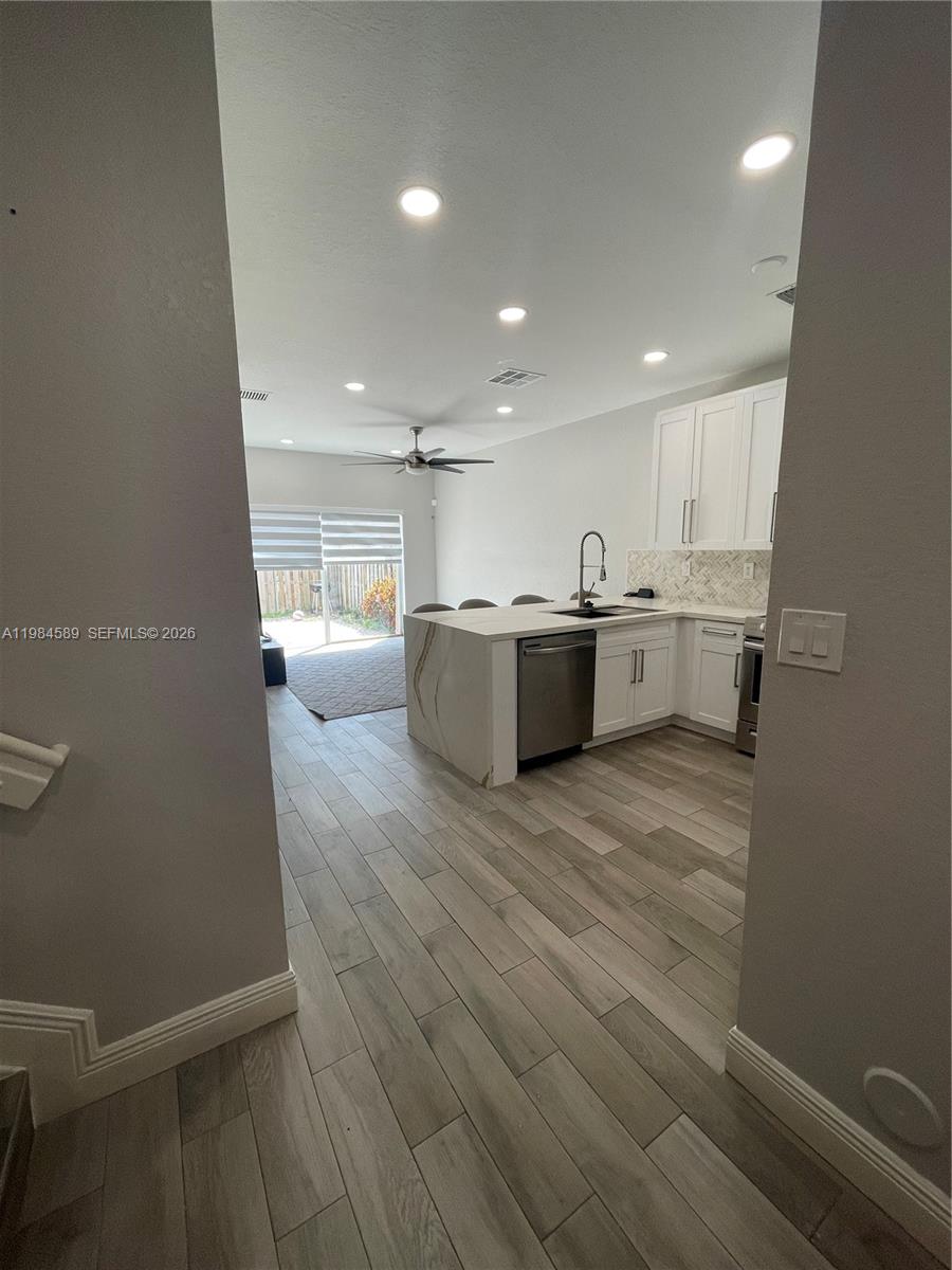 A modern kitchen with white cabinets and a waterfall island opens to a living area — 8900 SW 226th Ter, Cutler Bay FL 33190, CUTLER BAY, FL