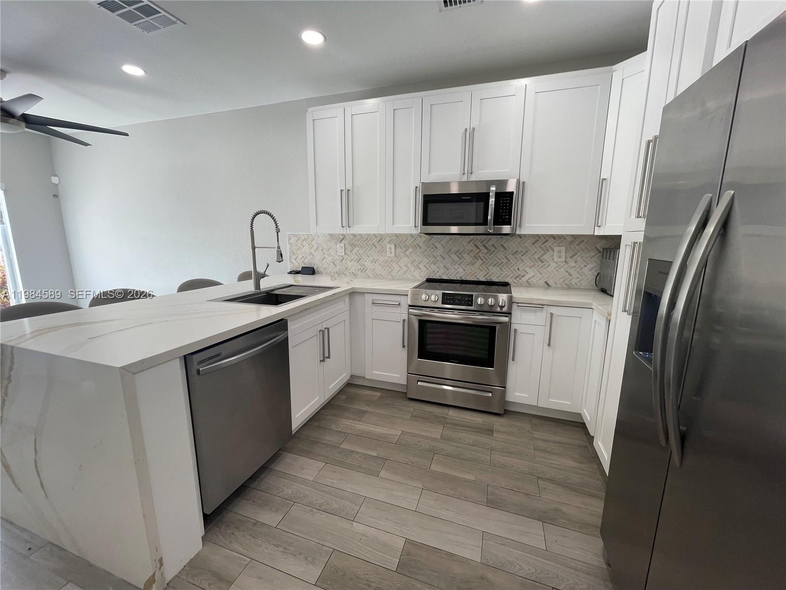 A modern kitchen features white cabinets, stainless steel appliances, and a waterfall-edge quartz island — 8900 SW 226th Ter, Cutler Bay FL 33190, CUTLER BAY, FL