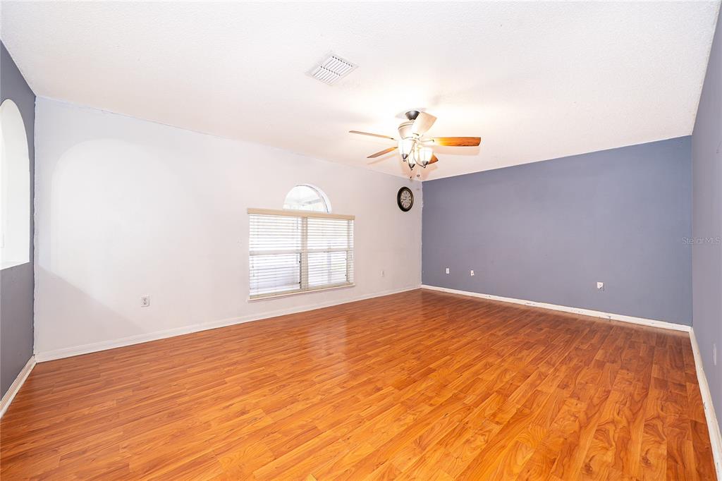 An empty room features wood-look flooring, a ceiling fan, and a blue accent wall — 10409 LAXTON STREET, ORLANDO, FL