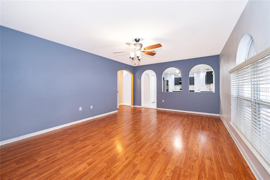 An empty living room features blue walls, wood-look flooring, a ceiling fan, and arched openings — 10409 LAXTON STREET, ORLANDO, FL
