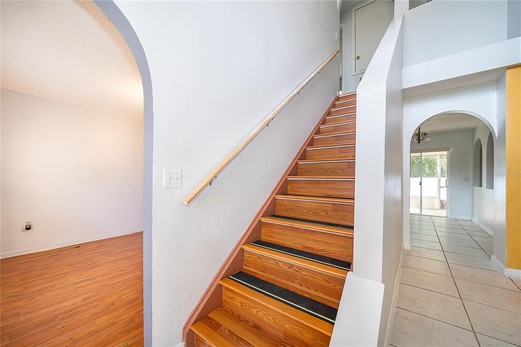 A wooden staircase with black tread strips sits between a laminate-floored room and tiled hallway — 10409 LAXTON STREET, ORLANDO, FL