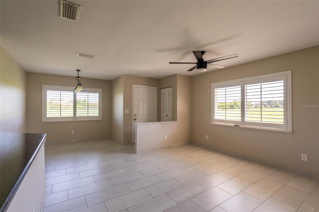 An open-concept room features light-colored tile flooring, a ceiling fan, and two windows with shutters — 5203 WATERVIEW WAY UNIT 5203, WINTER HAVEN, FL