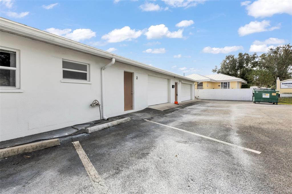 An exterior view of a white building with garage doors and a paved parking lot — 23263 HARBORVIEW RD, PORT CHARLOTTE, FL