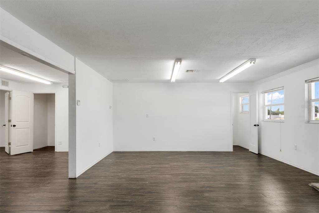 A bright, empty room with white walls, dark wood-look flooring, and two overhead fluorescent lights — 23263 HARBORVIEW RD, PORT CHARLOTTE, FL