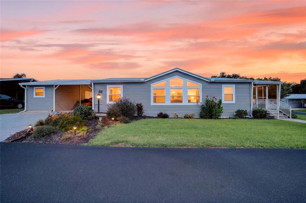 A single-story manufactured home with grey siding and a carport under a sunset sky — 11936 STANWOOD WAY, LEESBURG, FL