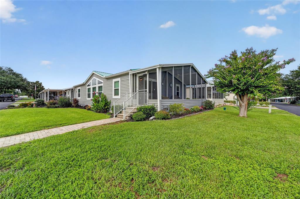 A single-story manufactured home features a screened-in porch and a paved walkway on grass — 11936 STANWOOD WAY, LEESBURG, FL