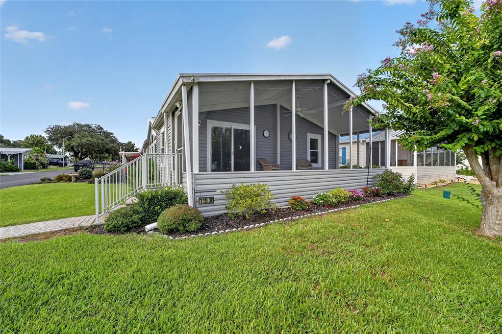 A single-story manufactured home features a screened-in porch, gray siding, and a landscaped front yard — 11936 STANWOOD WAY, LEESBURG, FL