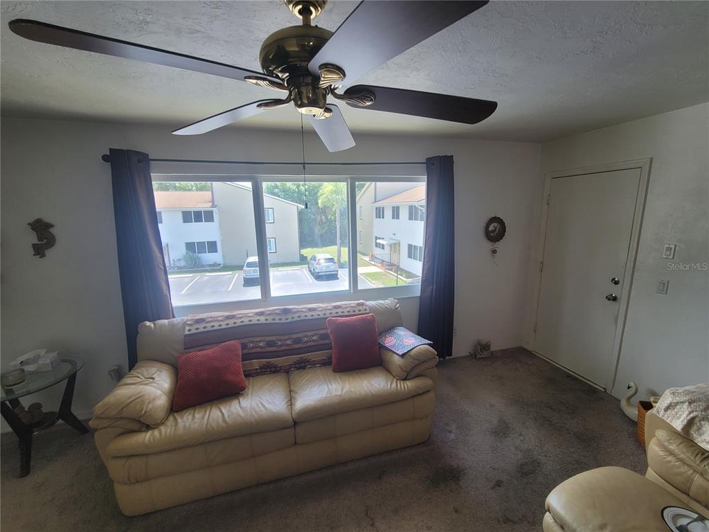 A living room features a beige sofa, a ceiling fan, and a large window view — 22481 WESTCHESTER BOULEVARD UNIT B40, PUNTA GORDA, FL