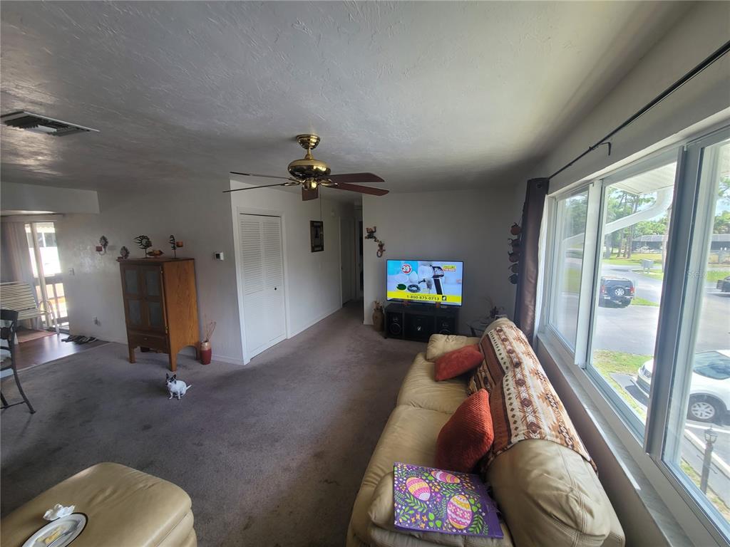 A living room features a beige sofa, a ceiling fan, and a large window — 22481 WESTCHESTER BOULEVARD UNIT B40, PUNTA GORDA, FL