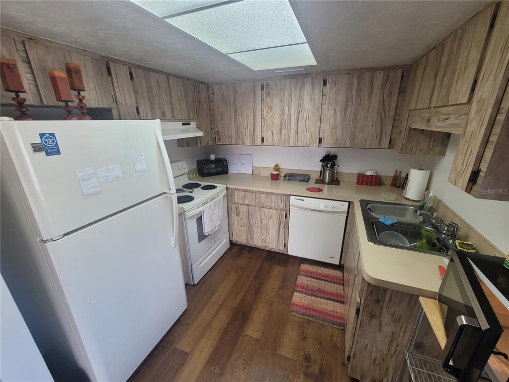A kitchen features wood-grain cabinets, white appliances, laminate countertops, and wood-look flooring — 22481 WESTCHESTER BOULEVARD UNIT B40, PUNTA GORDA, FL