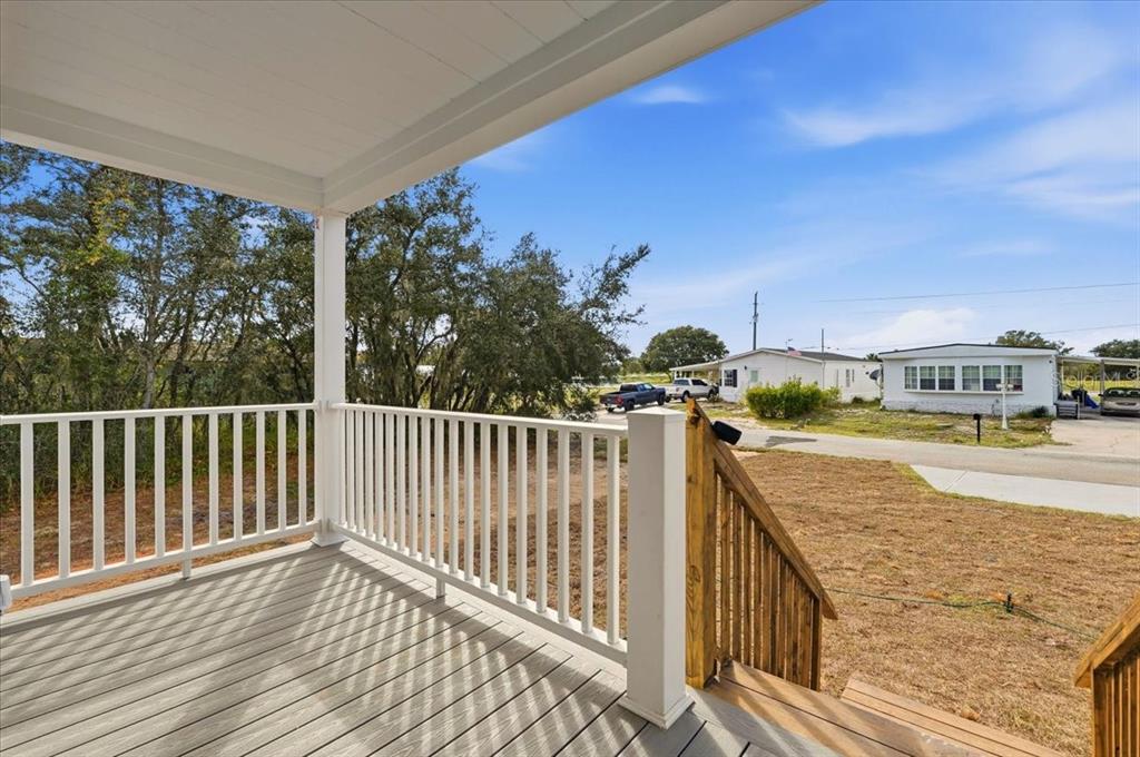 A wooden deck with white railings overlooks a yard and neighboring houses under a blue sky — 8400 BREEZE HILL DRIVE, LAKE WALES, FL