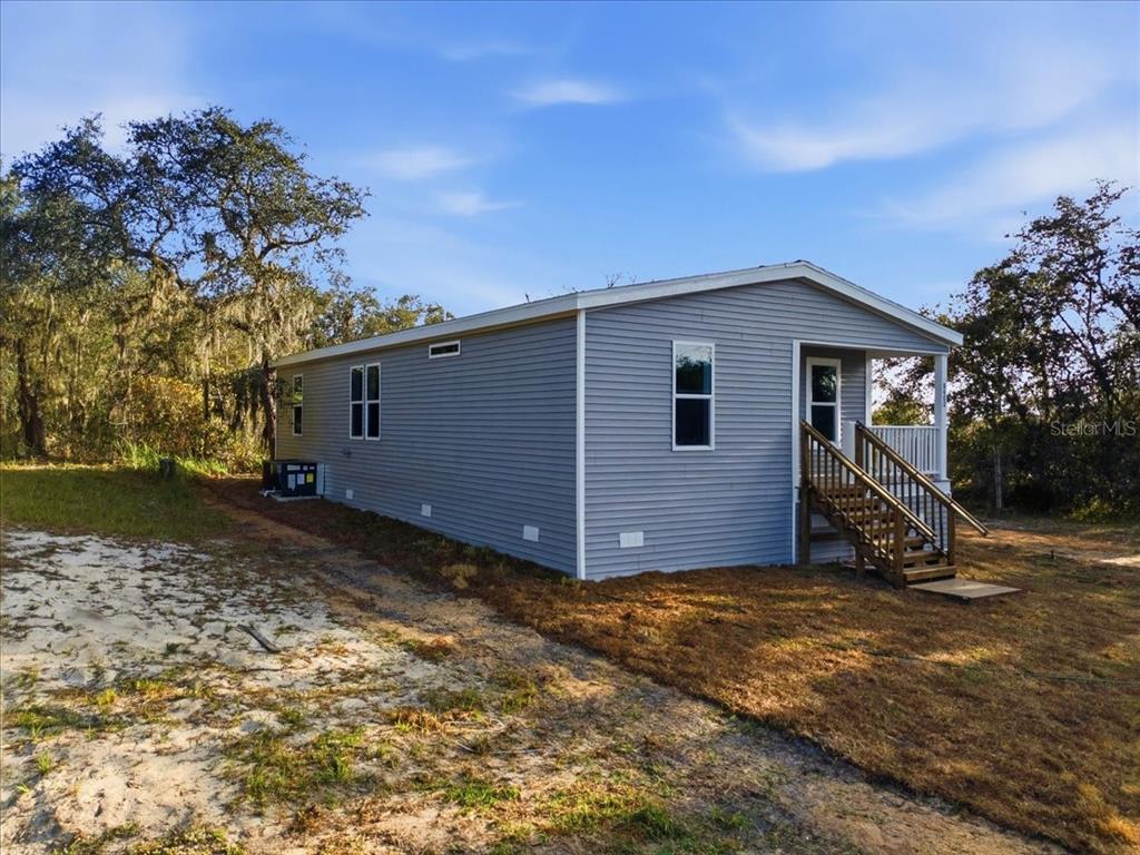 A gray manufactured home with a front porch and wooden stairs sits on a lot — 8400 BREEZE HILL DRIVE, LAKE WALES, FL